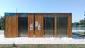 Das Foto zeigt ein flaches Gebäude aus Holz mit drei Edelstahltüren. Ganz links oben steht auf einem blauen Schild 
