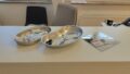 Foto aus dem Drogenkonsumraum KOMBO. Auf einem Tresen liegen zwei metallene Nierenschälchen, in denen verschiedene einwegverpackte Utensilien zu sehen sind: Ampullen mit Salzlösung, Löffel, im linken Schälchen eine Spritze, im rechten eine Crackpfeife. Rechts neben den beiden Schälchen liegt eine quadratische Spiegelscheibe, auf der ein kleines, leicht gebogenes Röhrchen und eine Plastikkarte liegen.