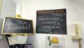 An einer Wand hängt eine schwarze Tafel, auf der in oranger Schrift steht:
