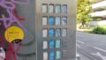 Detailaufnahme des Spritzenautomaten vor dem Eingang des KOMBO: Auf einer Reihe orangefarbener Tasten links ist in verblasster, abgeschnittener Schrift der Text „...pritzens... ...2 mm Kanül...“ zu erkennen, auf blauen Tasten daneben „...pritzens... ...3 mm Kanül...“. Auf mehreren weißen Tasten steht „Set Glaspfeife: Glaspfeife, Mundstück, Natron, Löffel, Sieb“, auf zwei grünen Tasten „Ascorbin und NaCl-W...“, auf einer weißen Taste „5 Kondome“. Links neben den Tasten sind auf dem Automaten Grafitti und ein runder Sticker zu erkennen, auf dem steht: „Nett hier. Aber hast du dich schon mal testen lassen?“